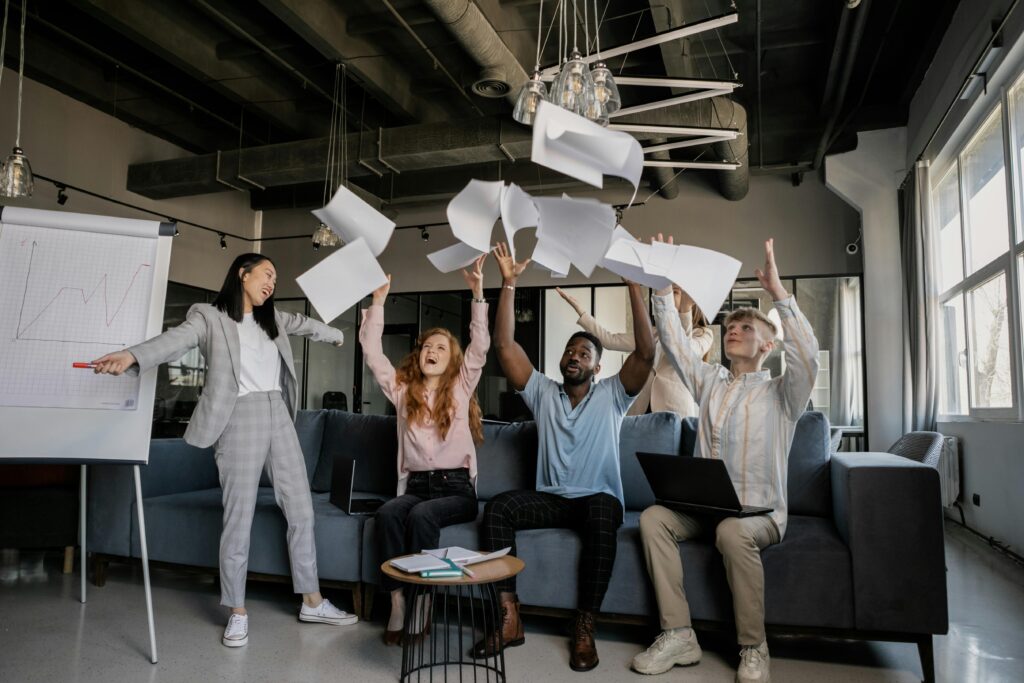 Diverse coworkers celebrate success by throwing papers in modern office setting.